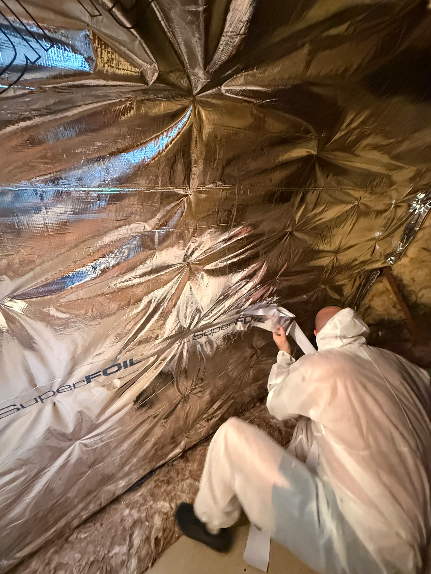 LoftServ Energy installer in protective suit taping SuperFOIL SF19+ multifoil insulation in a loft